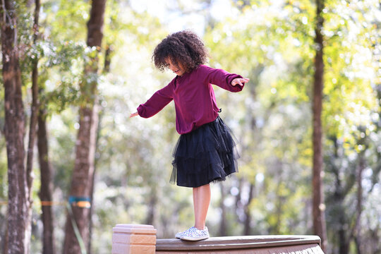 Young girl balancing on a wooden surface outdoors, arms outstret
