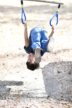 Child hanging upside-down on playground rings, smiling playfully