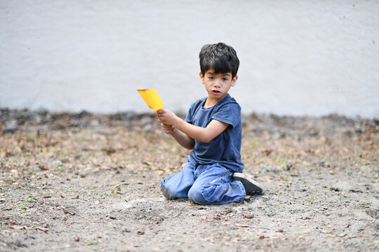 Young boy playfully tossing dirt with a yellow shovel outdoors.