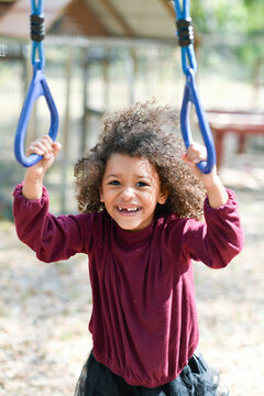 Smiling child gripping playground rings in a bright outdoor sett