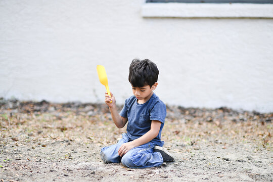 Young boy kneeling in dirt, holding a yellow shovel thoughtfully
