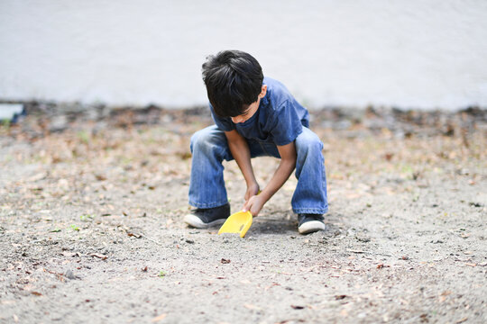 Young boy digging in dirt with a yellow shovel, focused on play.