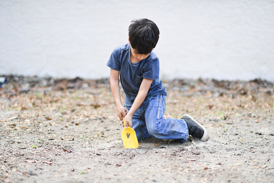 Young boy digging in the dirt with a yellow shovel, focused on p