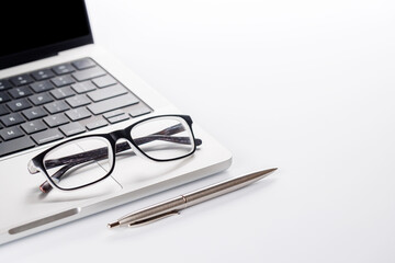 Closeup of an office table featuring a sleek laptop and reading glasses on a clean white surface