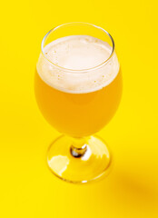 A frothy glass of fresh beer against a bright yellow background