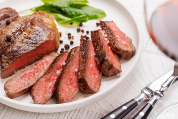 A perfectly cooked sliced striploin steak with a juicy, tender texture, served alongside a glass of rich red wine