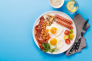 A classic breakfast plate featuring sunny-side-up eggs, crispy bacon, sausages, and fresh tomatoes