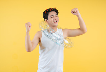 Portrait of a young Asian man wearing a tank top, swimming float and posing against a yellow background