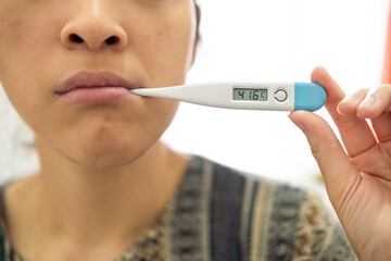 Digital thermometer showing high temperature held by person expressing discomfort, representative...