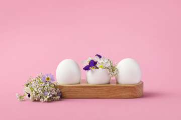 White eggs in wooden stand with spring pear and strawberry, purple viola flowers on a pink background. Happy Easter