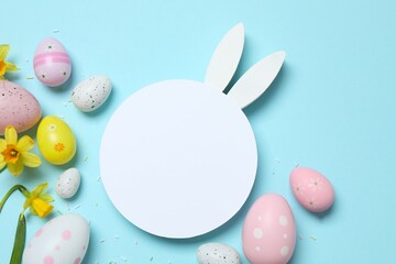 Happy Easter. Colorful eggs, bunny ears, paper card and yellow flowers on a pastel color background, space for text or advertising