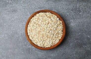 Wooden bowl with oatmeal flakes on gray background. Cooking breakfast