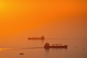 Obraz premium Sunset over ocean with cargo ship and small boats