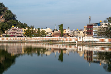 Shravanabelagola's tranquil lake reflecting the colorful buildings and hills in the distance during a clear day