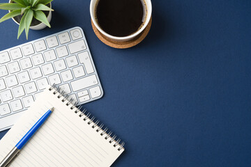 Workspace with keyboard, office supplies, pen, green leaf and coffee cup. Flat lay, top view blue...