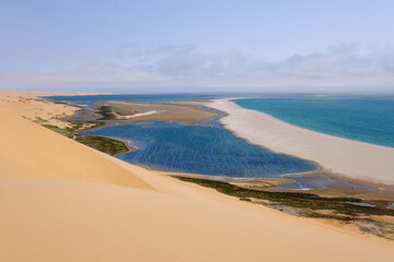 A mesmerizing view of where desert dunes embrace the ocean, with rich blue lagoons and golden sandbanks shaping the Namibian coastline.