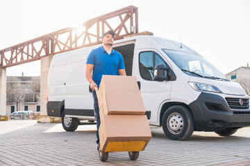 Delivery driver transporting packages with hand truck in front of van. Delivery driver concept in a...