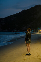 A woman stands on the sandy shore of Bình Ba Island at night, gazing at the gentle waves. The dim...