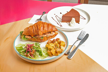 Brioche croissant grilled chicken sandwich served with sautéed vegetables with chocolate cheese cake in a cafe restaurant.