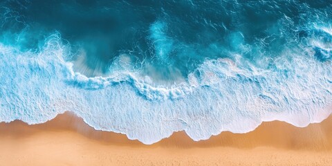 Fototapeta premium Aerial view of turquoise ocean waves crashing onto golden sandy beach creating a serene coastal landscape with vibrant light reflections above water.