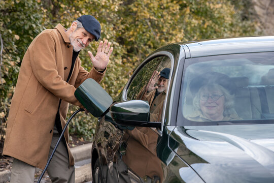 An elderly man waves to his wife in the passenger seat of thier EV
