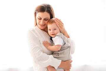a mother with a child, a young mother gently hugs and kisses her little son at home on a white isolated background, maternal love and care, a happy decree, a mother and a little boy, a place for text