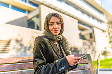 Muslim businesswoman using smartphone sitting on a park bench
