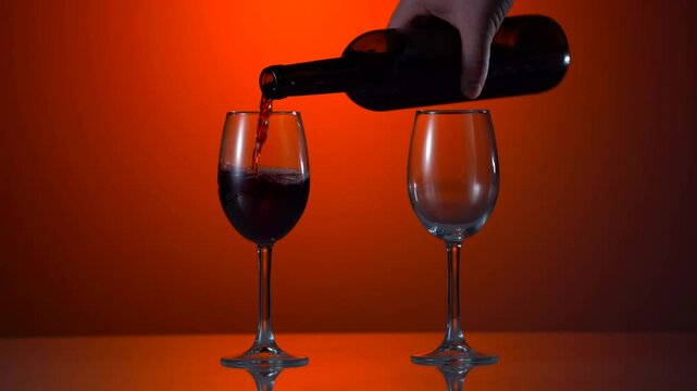 Pouring red wine from a bottle into two glasses on the vineyards in Sicily. Sommelier pouring red wine in glass with Etna volcano at background. Close-up of filling wine glass with red wine