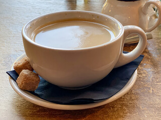 Americano coffee served with milk and two brown sugar cubes in a cup and saucer on wooden table