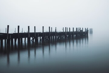 Fototapeta premium Serene, foggy pier extending into calm waters, creating a tranquil and mysterious atmosphere.