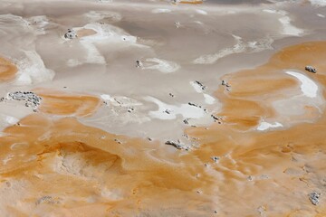 Aerial view of a barren desert landscape with orange and white mineral deposits creating patterns.