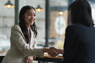 Obraz premium Two businesswomen shaking hands after a successful meeting in a modern office, showcasing collaboration and partnership while exuding confidence and professionalism