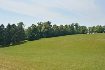 Obraz premium A serene view of Cmrok in Zagreb, Croatia, featuring a vast, gently sloping green field bordered by lush trees under a partly cloudy sky