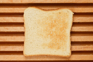 A slice of toast is centered on a wooden cutting board, showcasing its golden-brown color and slightly uneven texture