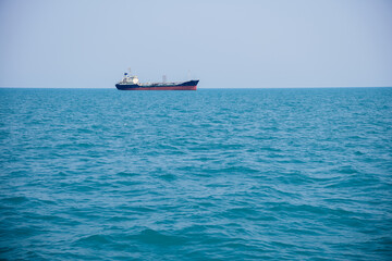 Cargo ship sailing across a vast, calm blue sea under a sunny sky, creating a peaceful scene of maritime transport and exploration