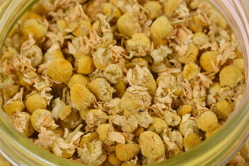 A close-up shot of dried chamomile flowers an a glass jar, showcasing their delicate petals and yellow centers.