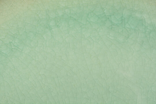 A close-up shot of a ceramic plate detail with a light green glaze and subtle crackle pattern