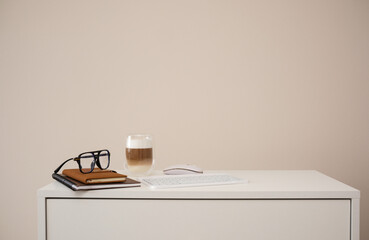 A serene workspace with a latte, notebooks, and stylish glasses on white table.