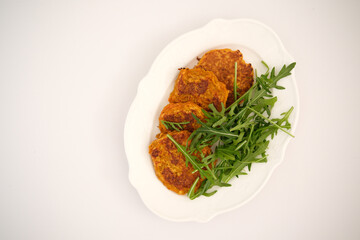 Carrot pancakes with rucola on white plate.