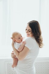 A happy young mother and a newborn baby smile, hug and kiss on a white isolated window background, a loving family at home