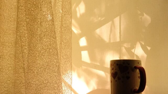 Cup of tea or coffee at the morning, Light and floral shadow, soft blurred sunlight flares. Vintage textile background. Abstract backdrop with crossed lines shadows. Wabi sabi style aesthetics. 
