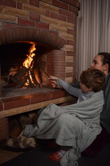 Obraz premium A young parent and child enjoy cozy leisure time by the fireplace, embracing the warmth and comfort of winter time indoors. Hygge concept. Family bonds and shares precious moments together at home