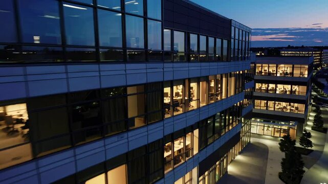 Modern office building illuminated at dusk with landscaped gardens and walkways