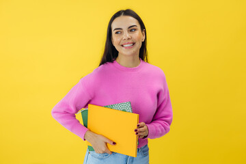 Intelligent brunette woman student enjoying studying and achieving new skills and knowledge. Holding books on yellow background