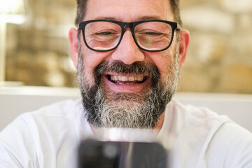 Cheerful adult man indoors at home, using his smartphone for a video call, smiling and laughing...