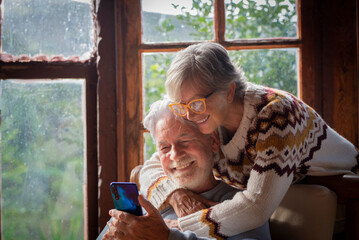 Senior couple operate cellphone in chalet during winter vacation via smartphone apps contacting...
