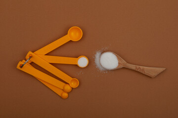 Glucono-delta-lactone (GDL), also known as gluconolactone. Food additive E575 in measuring spoons on brown background. White powder, oxidized derivative of glucose. Acidity regulator, baking powder