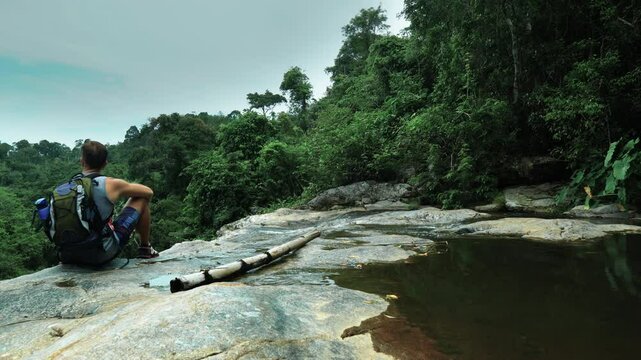 A tourist sits at the cliff of a mountain waterfall in the jungle
