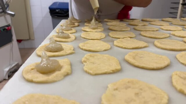 A pastry chef filling with a piping bag handmade Spanish traditional sweet potato fritters on a marble table. 4K