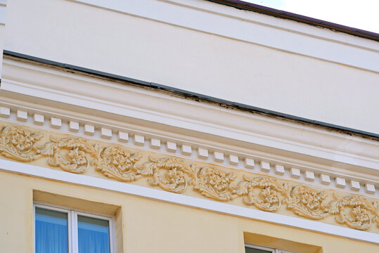 Stucco ornament with floral patterns and dentils on the exterioron of historical building facade. Decorative stucco molding with floral relief patterns, classical design and historical craftsmanship